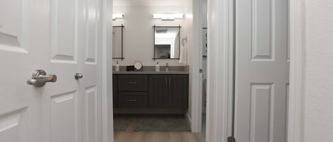 A hallway leading to a bathroom with a vanity, mirror, and towel rack.
