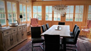 A dining area with a wooden table, black upholstered chairs, a patterned rug, and a large window with a view of greenery. - Vacation apartment Sonnenblick Deluxe ground floor (Reit im Winkl)