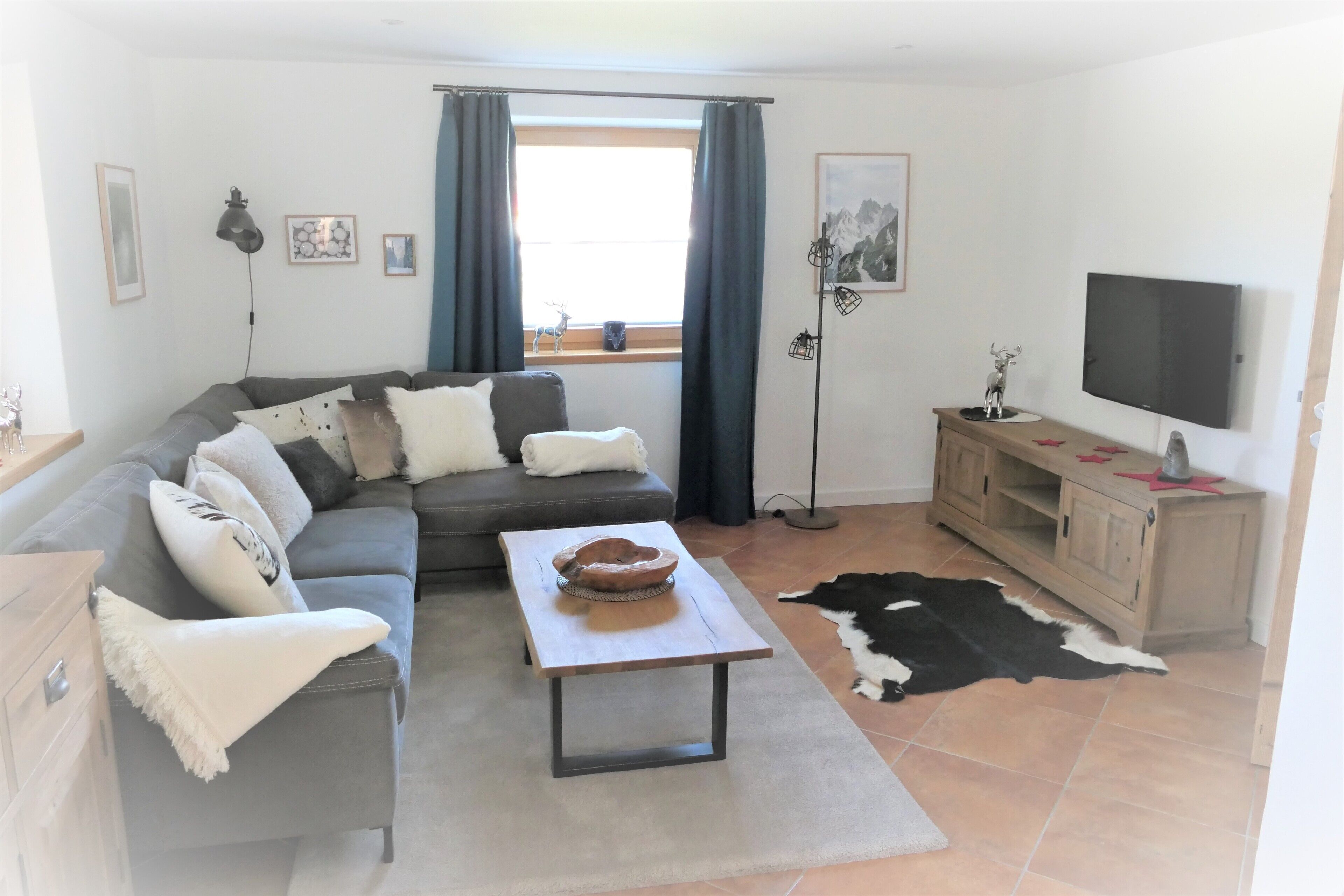 Een moderne woonkamer met een grijze bank, een salontafel, een televisie en een houten kast.