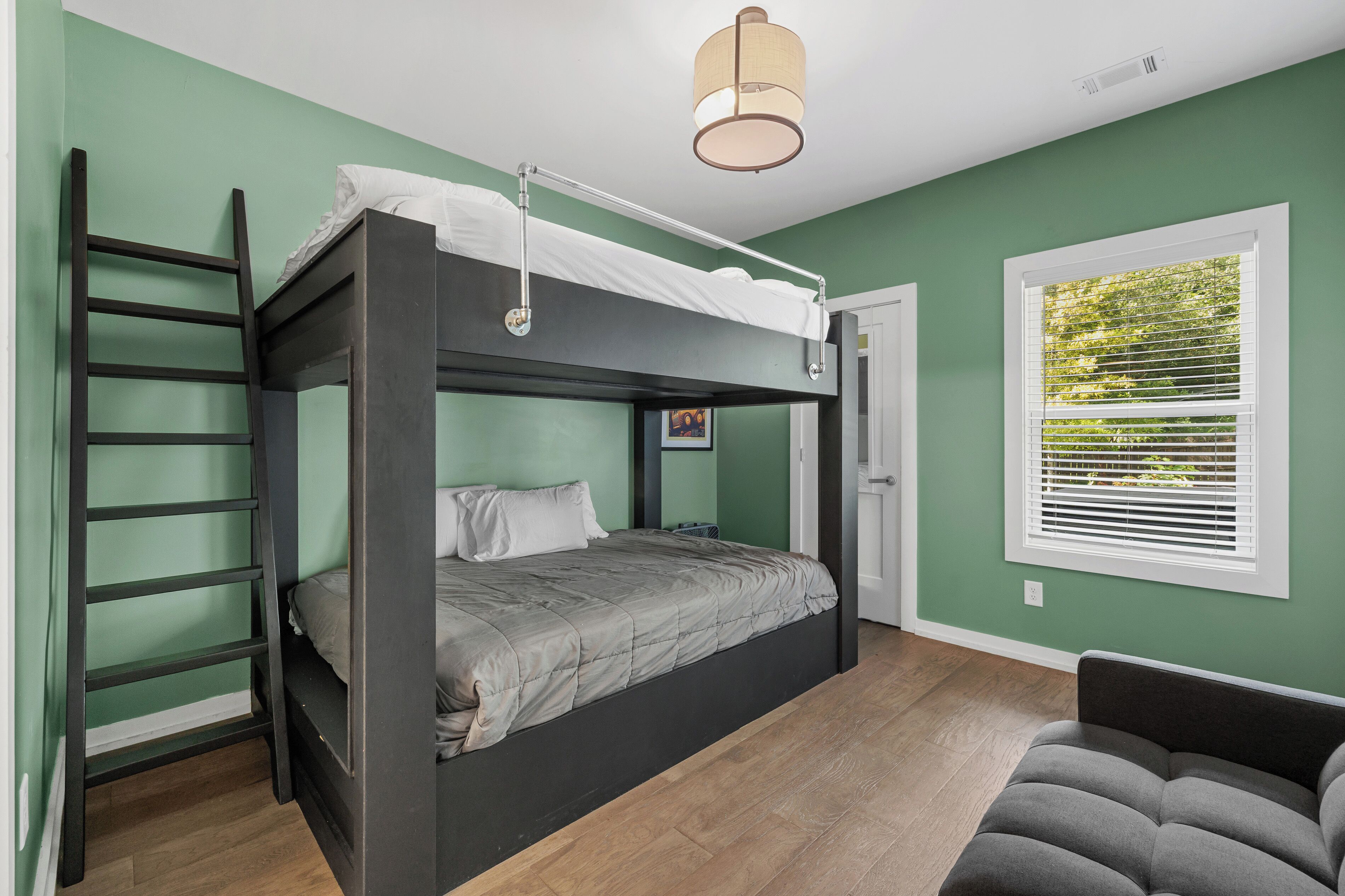 A bunk bed with a ladder, a bedside table, and a window with blinds.