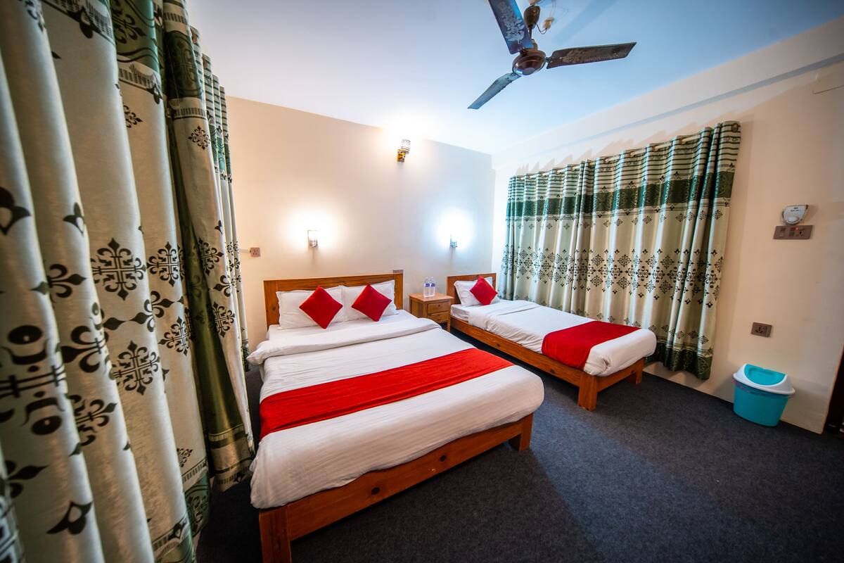 A hotel room with two beds, a ceiling fan, and patterned curtains.