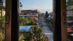 Vista a través de una ventana que muestra una calle con edificios, cielo despejado y montañas al fondo.