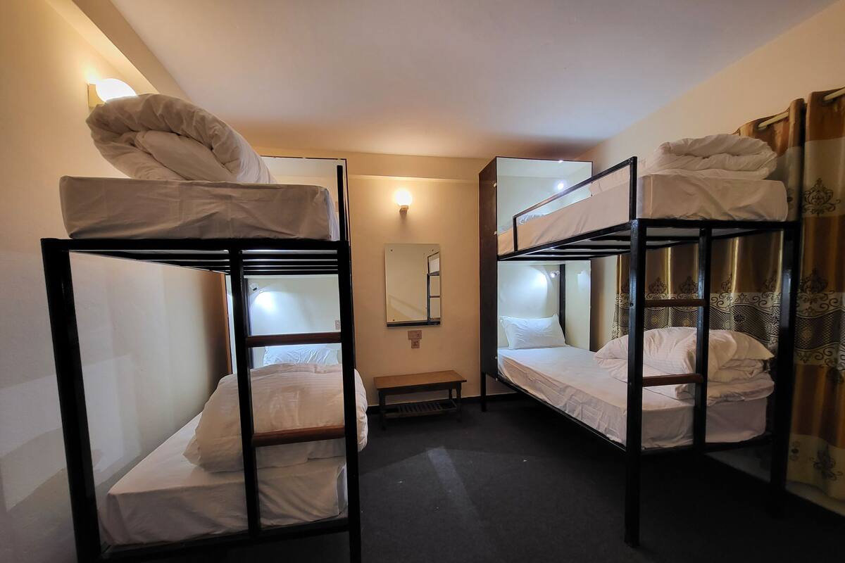 A dormitory room with bunk beds, a small bench, and a wall-mounted mirror.