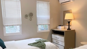 Ein Hotelzimmer mit zwei Betten, einem Nachttisch, einer Lampe, einem Schminktisch und einer Klimaanlage.