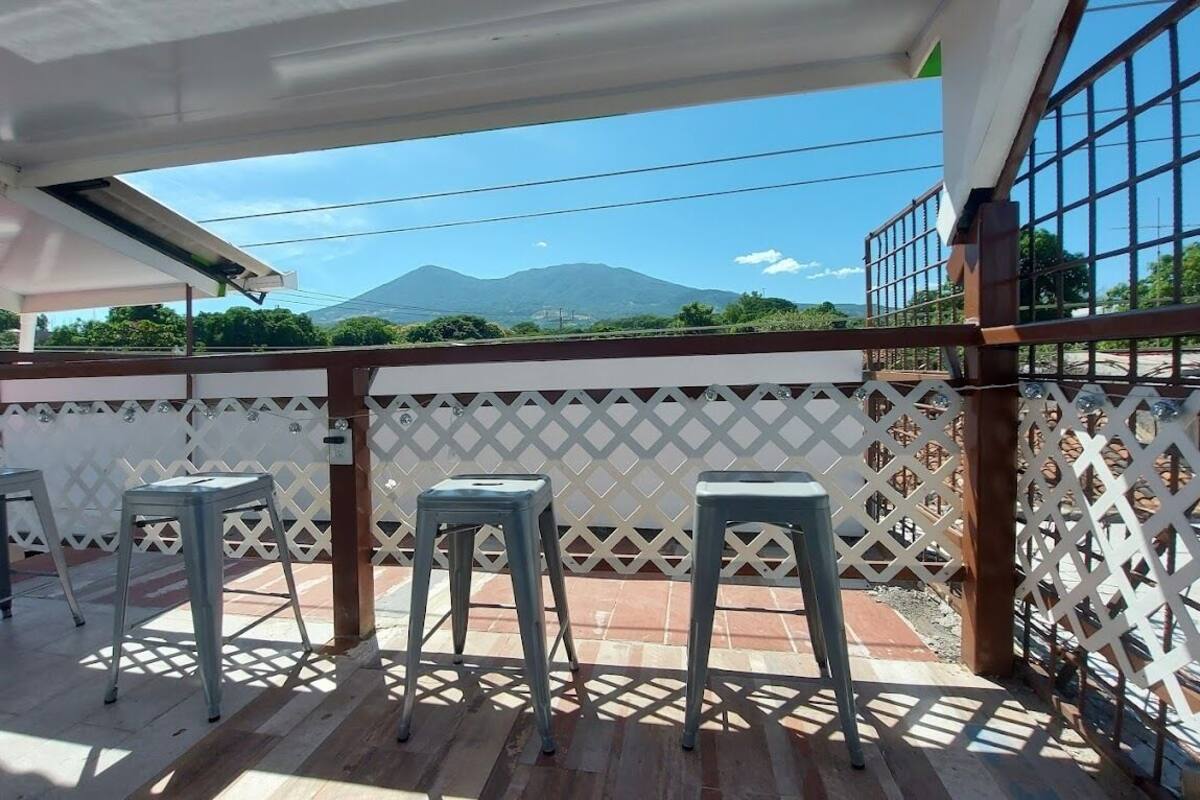 A balcony with three metal stools, a white lattice fence, and a view of mountains.