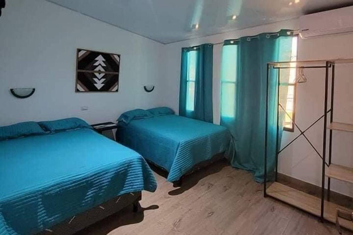 A room with two beds, a wall-mounted shelf, and a window with curtains.