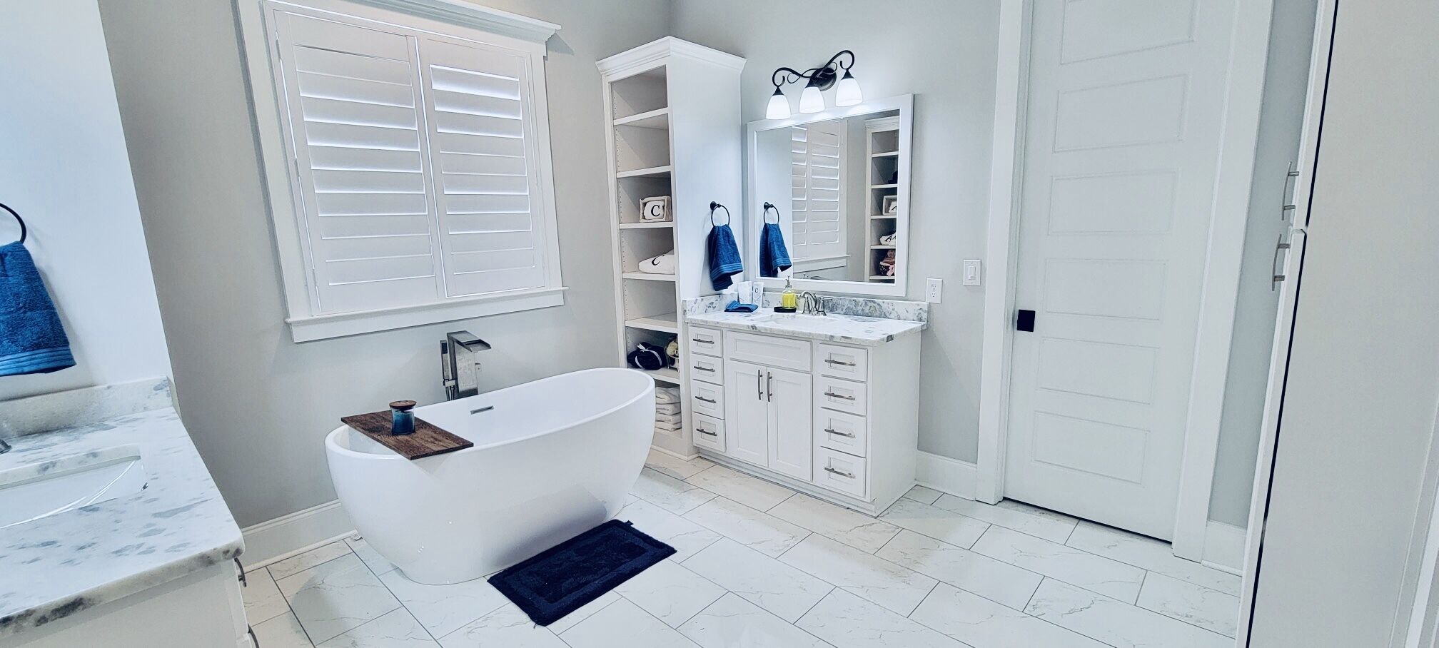 A modern bathroom with a freestanding bathtub, a vanity with a mirror, and a built-in shelving unit.