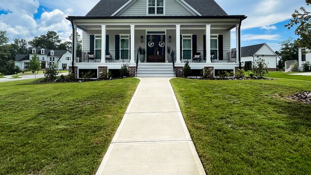 Une maison à deux étages avec un porche à l’avant, une allée et une pelouse bien entretenue.