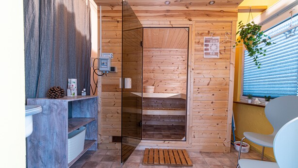 Un sauna en bois doté d’une porte en verre, d’un banc en bois et d’une petite étagère sur laquelle sont posés divers objets.
