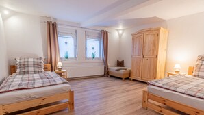 Une chambre avec deux lits en bois, une armoire, une fenêtre avec des rideaux et une petite table avec une lampe.