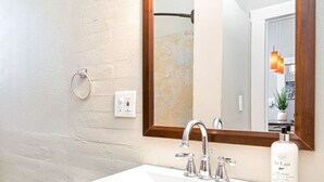 A bathroom with a white sink, two faucets, a mirror, and a hand wash bottle.