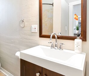A bathroom with a white sink, two faucets, a mirror, and a hand soap dispenser.