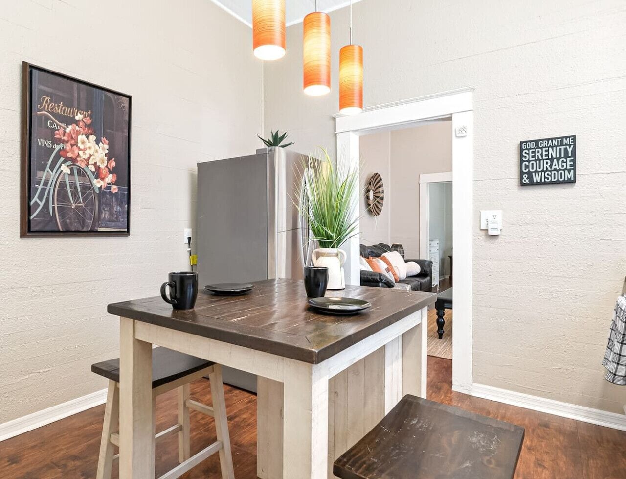 Una cocina moderna con una isla de madera, luces colgantes, un menú enmarcado y una frase motivacional en la pared.