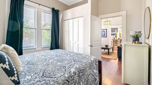 A bedroom with a bed, a door leading to a living area, and a view of the outside.
