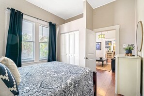 A bedroom with a bed, a door leading to a living area, and a view of the outside.