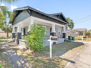A single-story house with a covered porch, a mailbox, and a small tree in the yard.