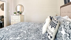 A bedroom with a patterned bedspread, a dresser with a mirror, and a bedside table with a lamp.