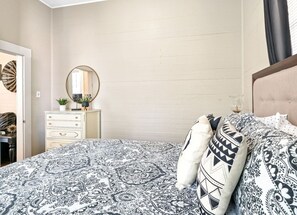 Een slaapkamer met een bedovertrek met patroon, een dressoir met spiegel en een nachtkastje met lamp.