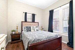 Een slaapkamer met een houten bed, een nachtkastje, een lamp en een raam met gordijnen.