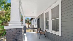 A covered porch with a stone column, a table with chairs, and a potted plant.