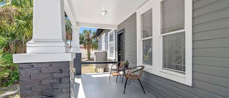 A covered porch with a stone column, a table with chairs, and a potted plant.