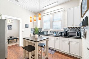 Una cocina con armarios blancos, encimera negra y microondas.