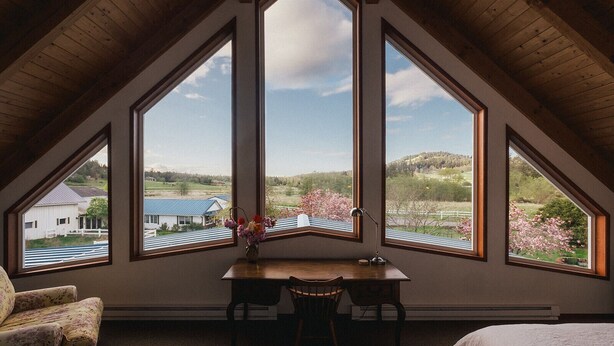 A room with a sloped ceiling and large windows offering a view of a rural landscape. - Saturn's Return (Friday Harbor)