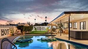 Een zwembadgedeelte met ligbedden en parasols, een jacuzzi en een bord met de tekst 'wish you were here'.