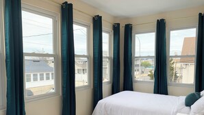 Un dormitorio con dos camas, ventanas grandes con cortinas y vistas al exterior.