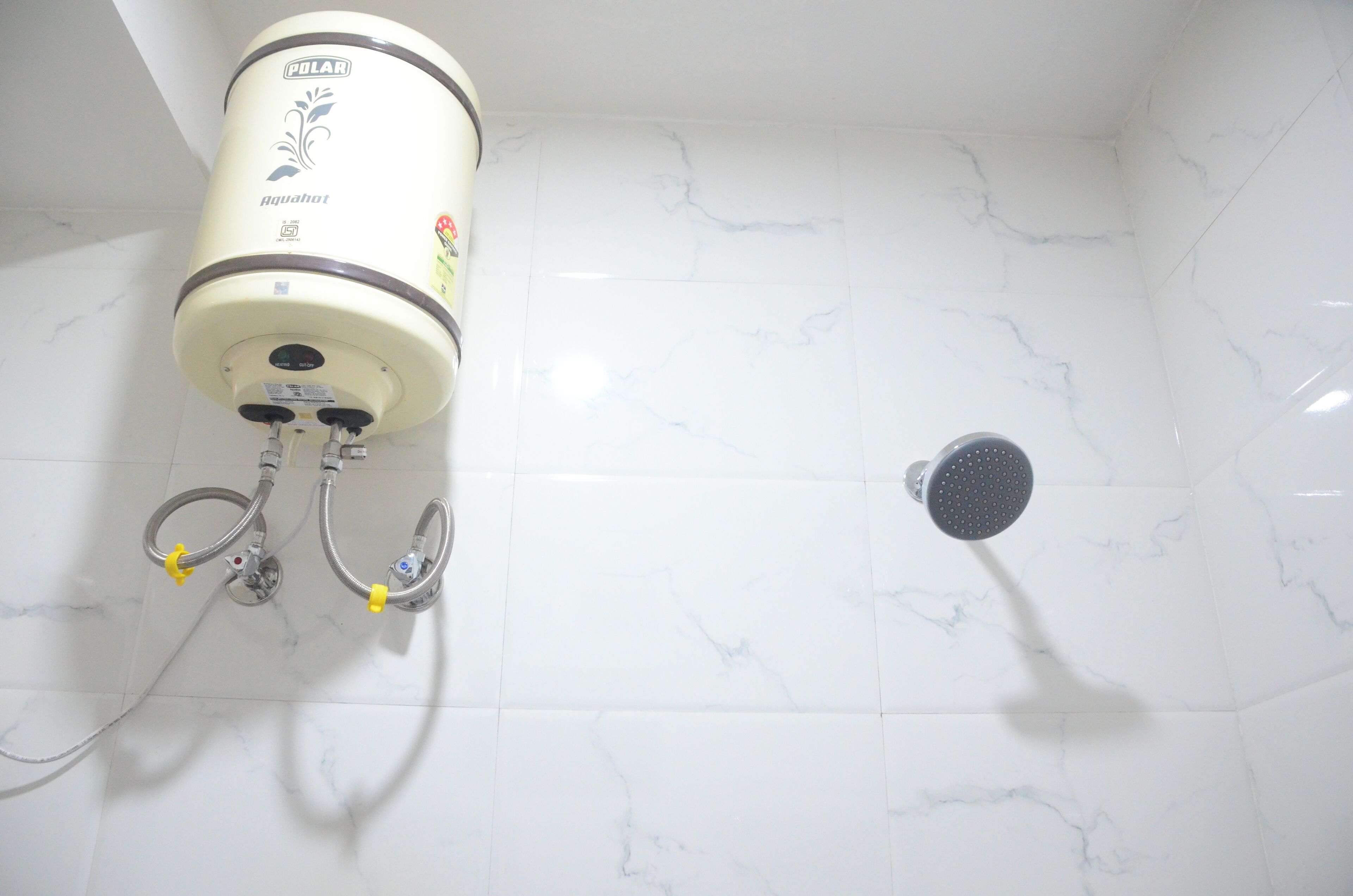 A bathroom with white marble tiles, a showerhead, and a water heater labeled "Polar Aquahot."
