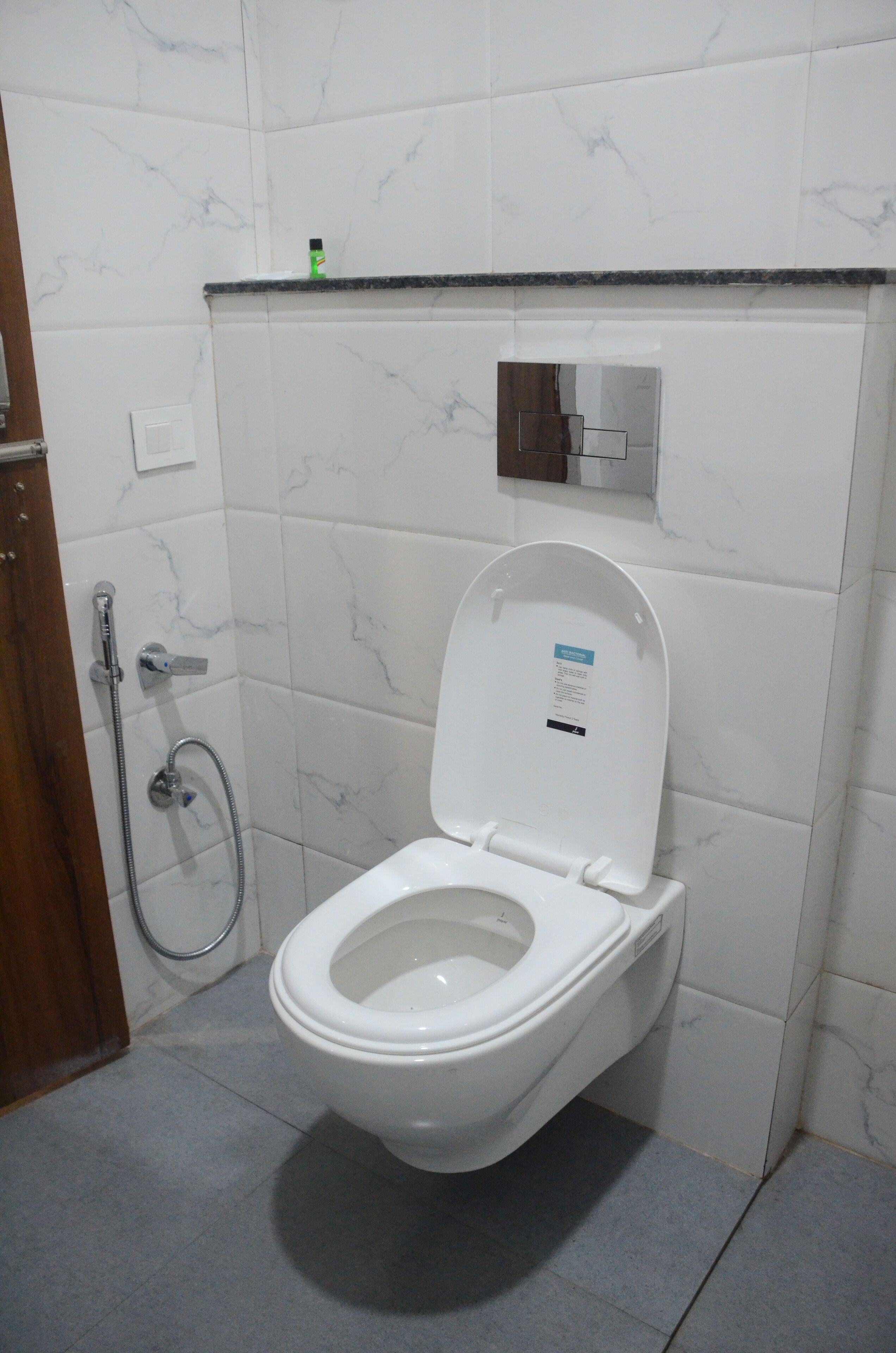 Une salle de bain avec des toilettes blanches, une douche et un mur recouvert de carreaux de marbre.