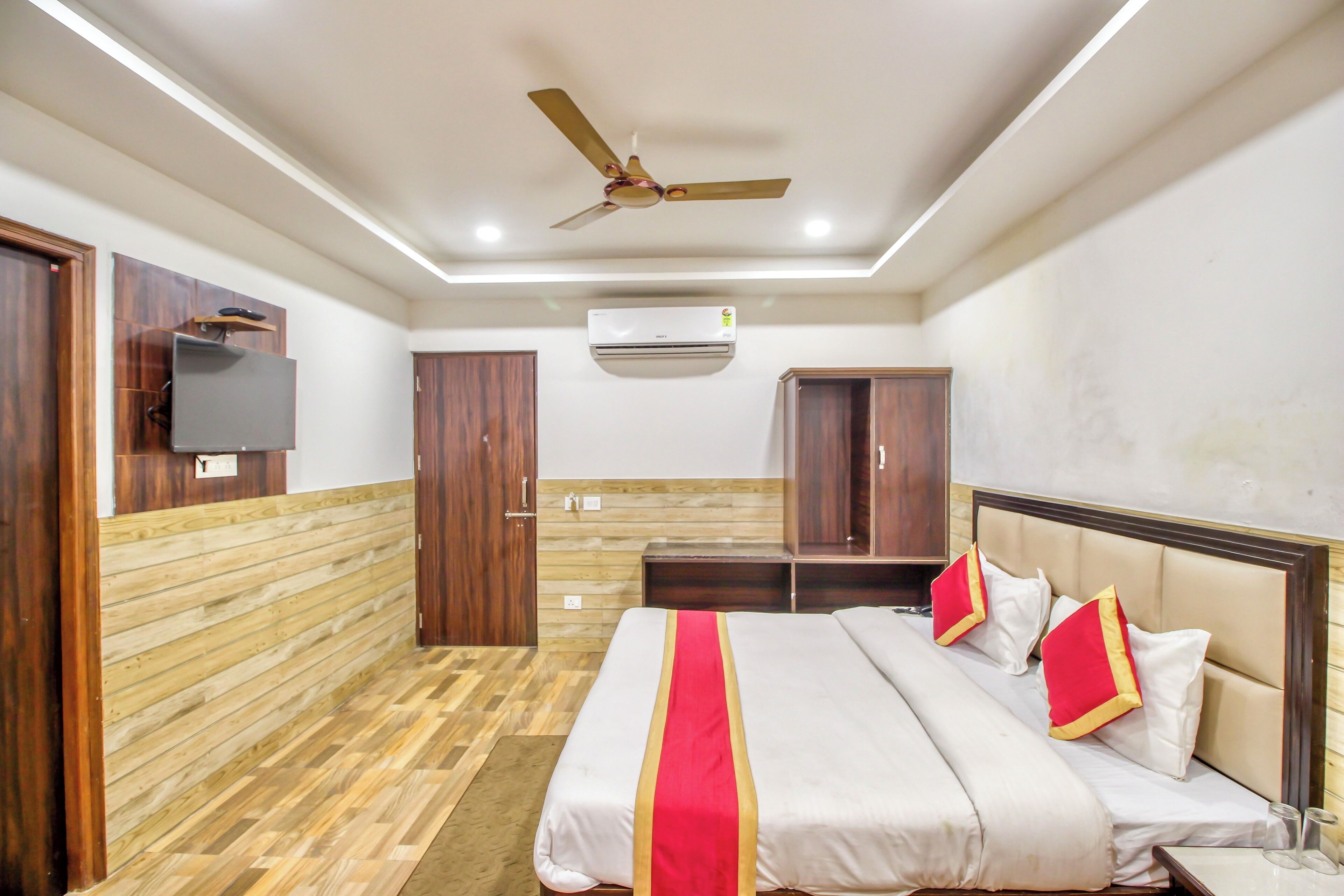 Une chambre d’hôtel avec un lit, des lambris en bois, un ventilateur de plafond, un appareil de climatisation et un téléviseur fixé au mur.