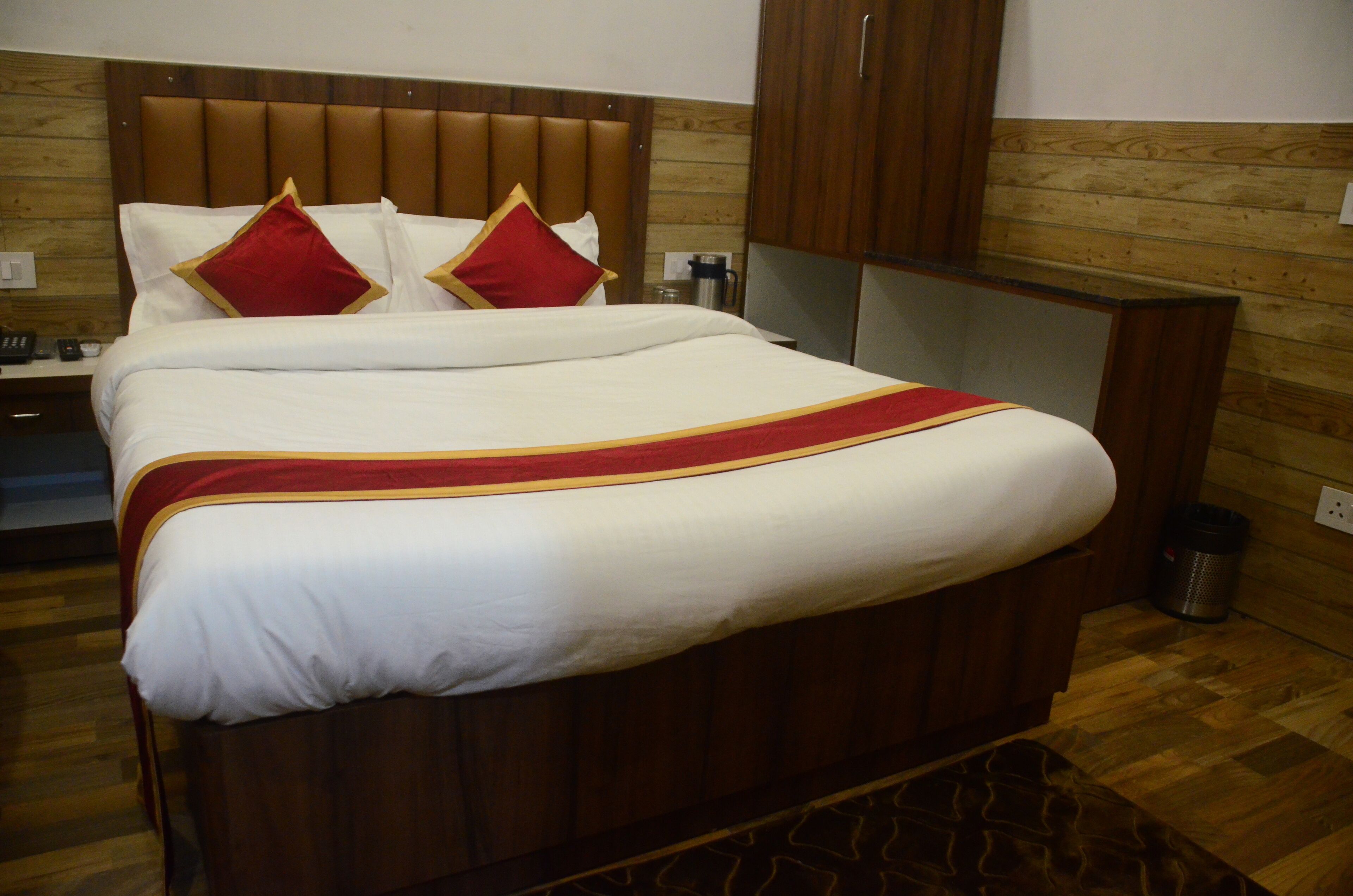 Una cama bien hecha con colcha roja y dorada, cabecero de madera y un armario de madera en una habitación de hotel.