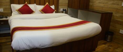 Una cama bien hecha con colcha roja y dorada, cabecero de madera y un armario de madera en una habitación de hotel.