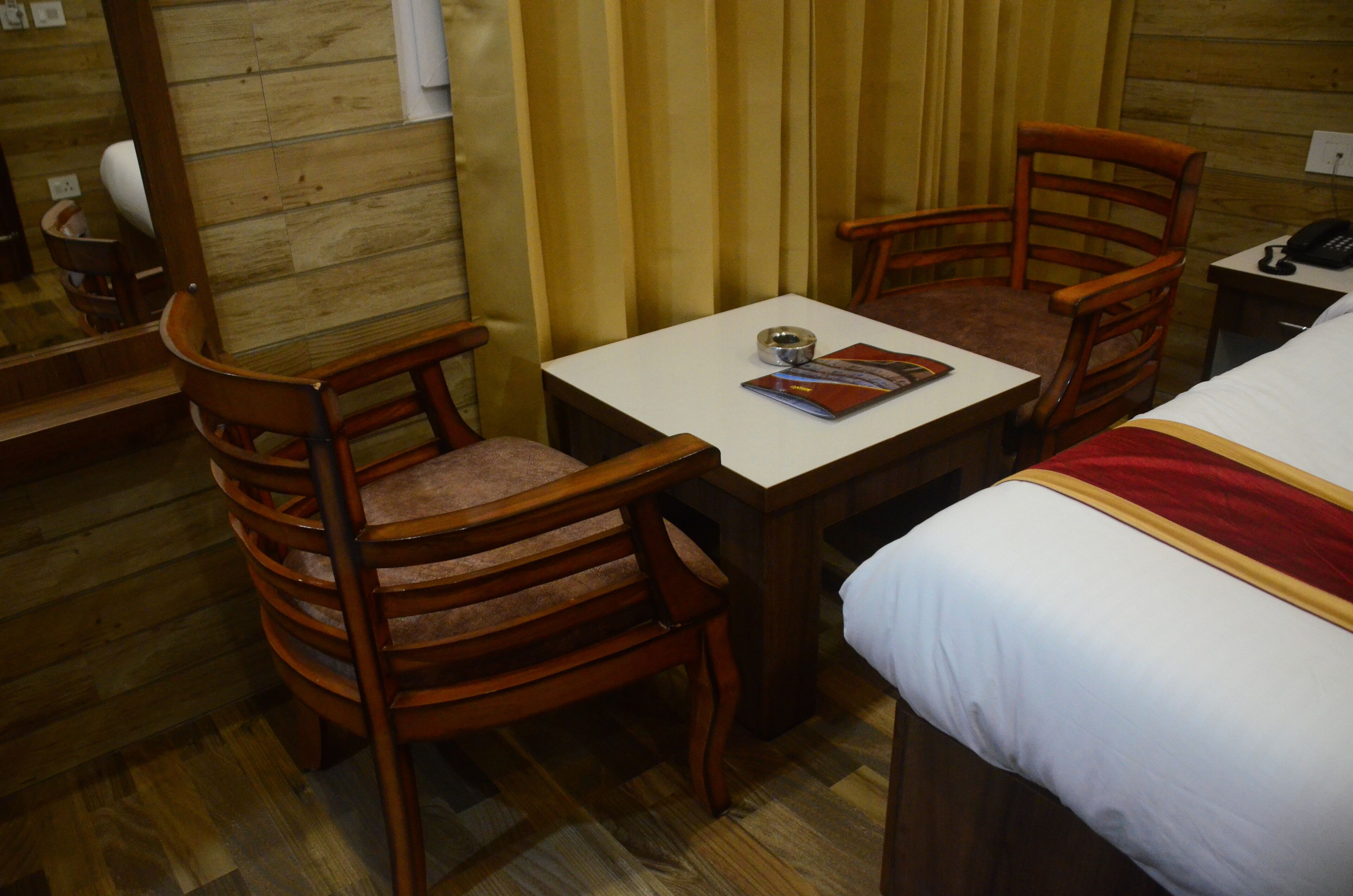 A wooden room with a bed, two wooden chairs, a small table, and a mirror.