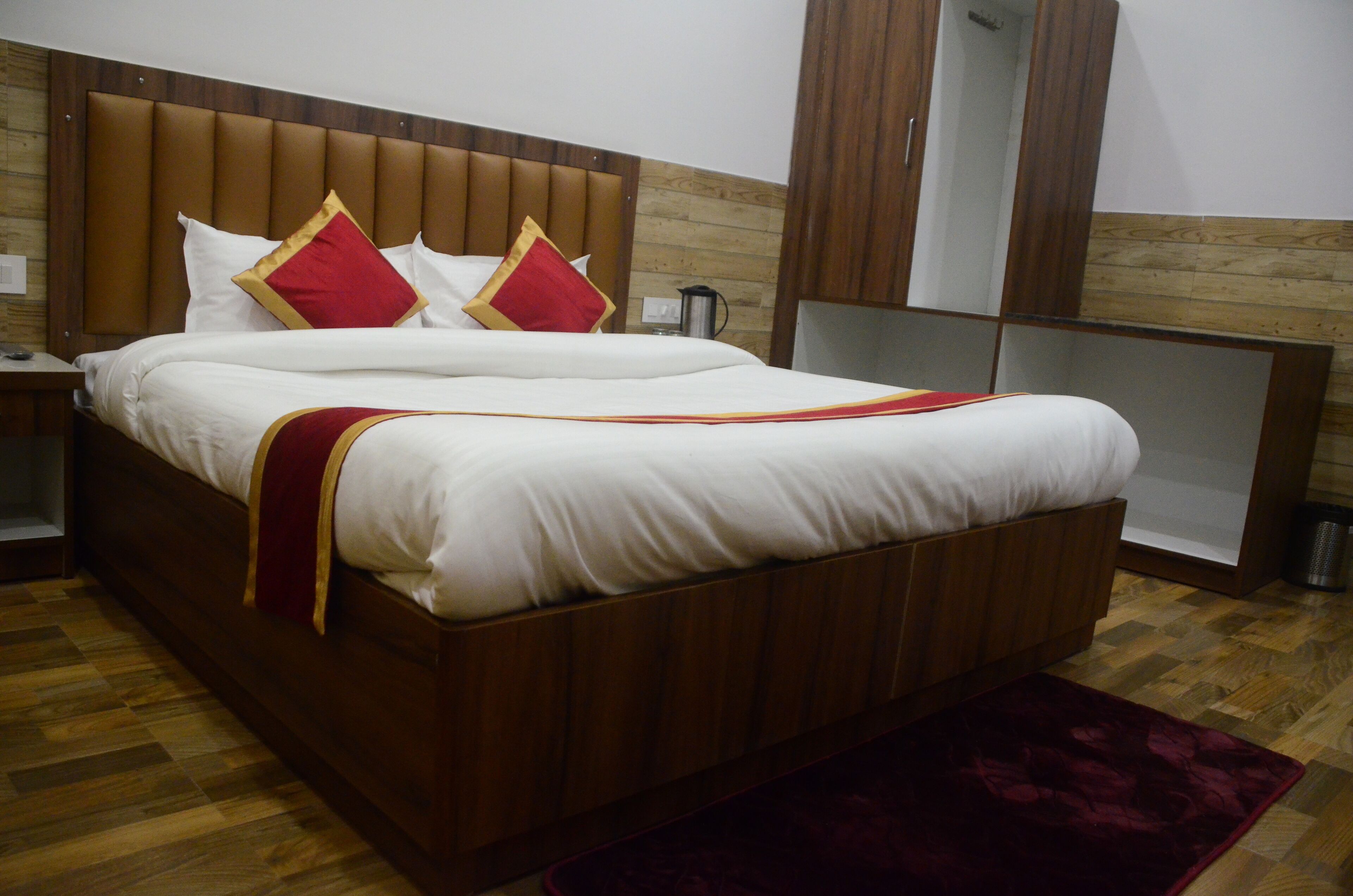 A large bed with a wooden headboard, white bedding, and red and gold pillows.