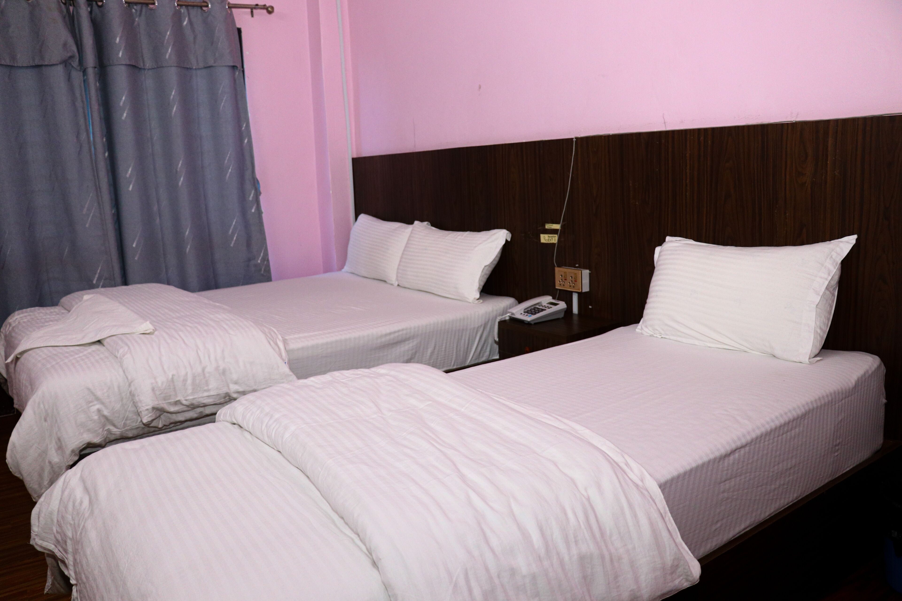 A hotel room with two single beds, a wooden headboard, a bedside telephone, and a curtain.