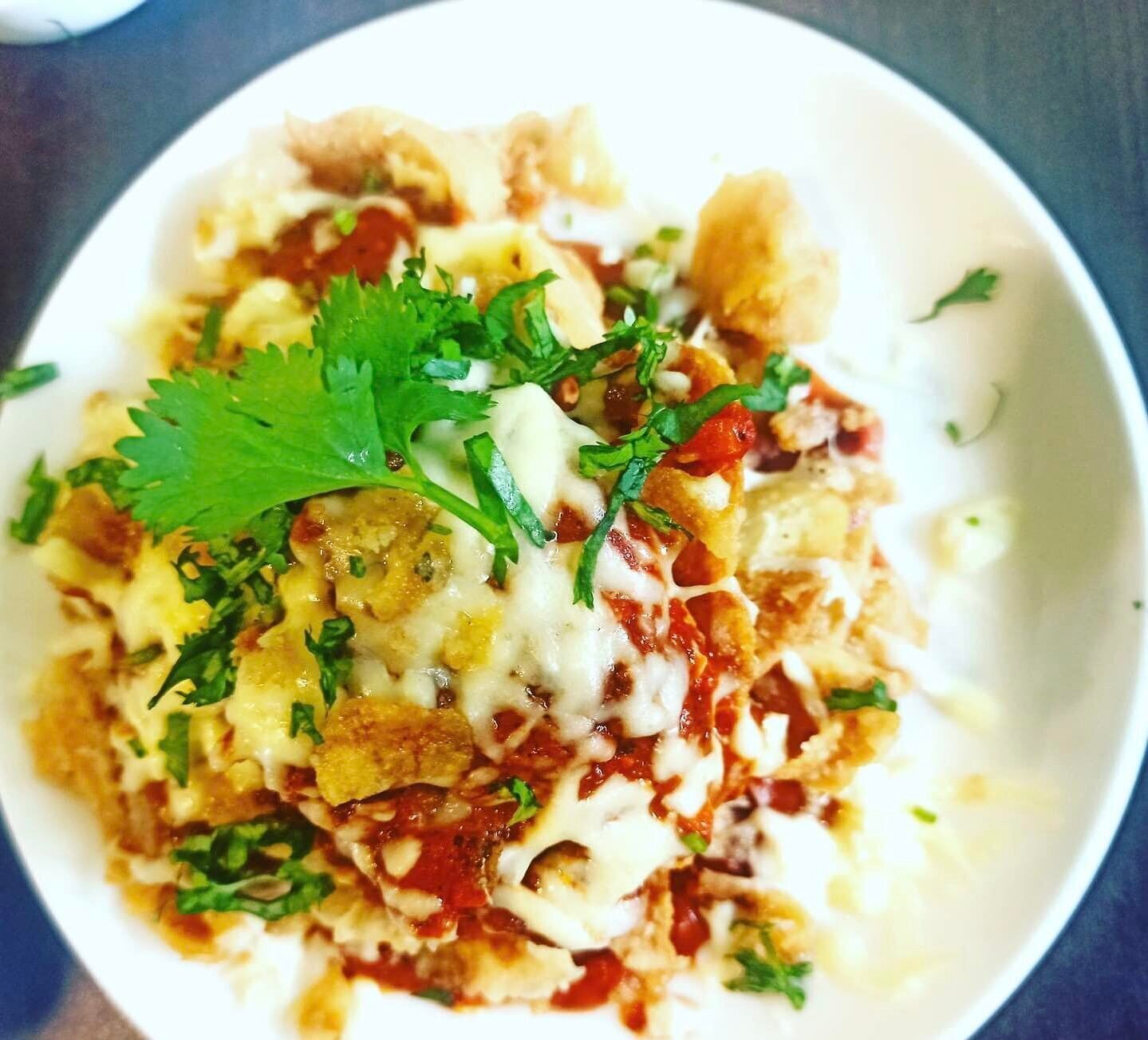 Uma tigela de nachos cobertos de queijo, tomate e coentro.