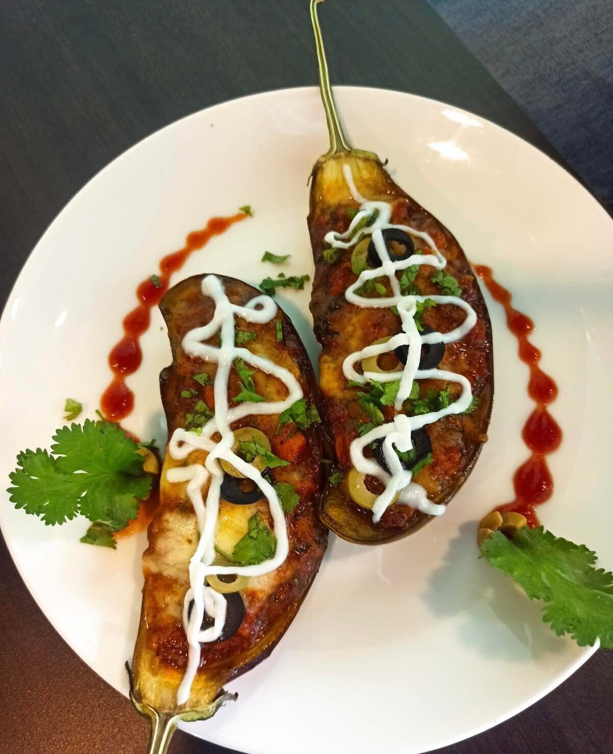 Two grilled eggplants on a white plate with white sauce drizzles and garnished with cilantro.