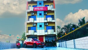Un immeuble à plusieurs étages, sur lequel on peut lire l’inscription « HÔTEL YES Pvt. Ltd. », et une voiture rouge garée devant.