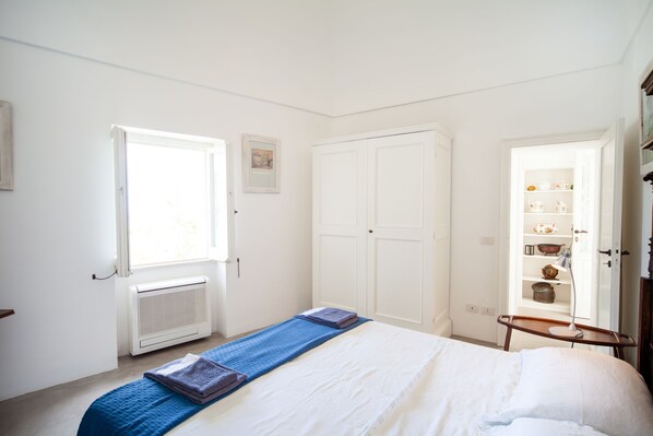 A bedroom with a bed, a window, a radiator, a wardrobe, and a shelf with items. - Casa Eolo - Capri center (Capri)