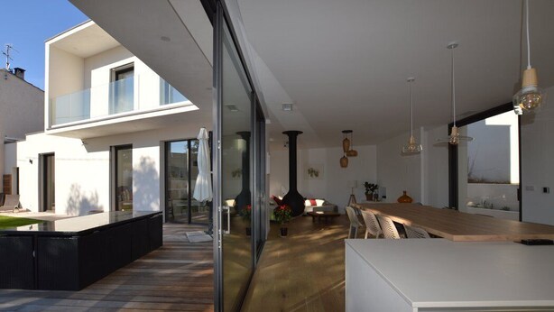 A modern kitchen with a large island, a dining area with a wooden table, and a glass-enclosed patio area.