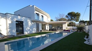 A modern two-story house with a swimming pool, a patio, and a well-maintained lawn.