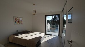 A modern bedroom with a large bed, a sliding glass door to a balcony, and a wall-mounted artwork.
