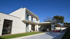 A modern two-story house with a large patio area, a covered outdoor seating space, and a well-maintained lawn.