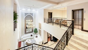 A spacious foyer with a grand staircase, a seating area with a chandelier, and a modern elevator. - Maison Privee - Majestic Resort Villa with Private Pool on The Palm (Dubai)