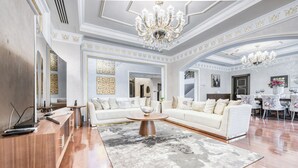 A spacious living room with a large white sectional sofa, a wooden coffee table, and a chandelier. - Maison Privee - Majestic Resort Villa with Private Pool on The Palm (Dubai)