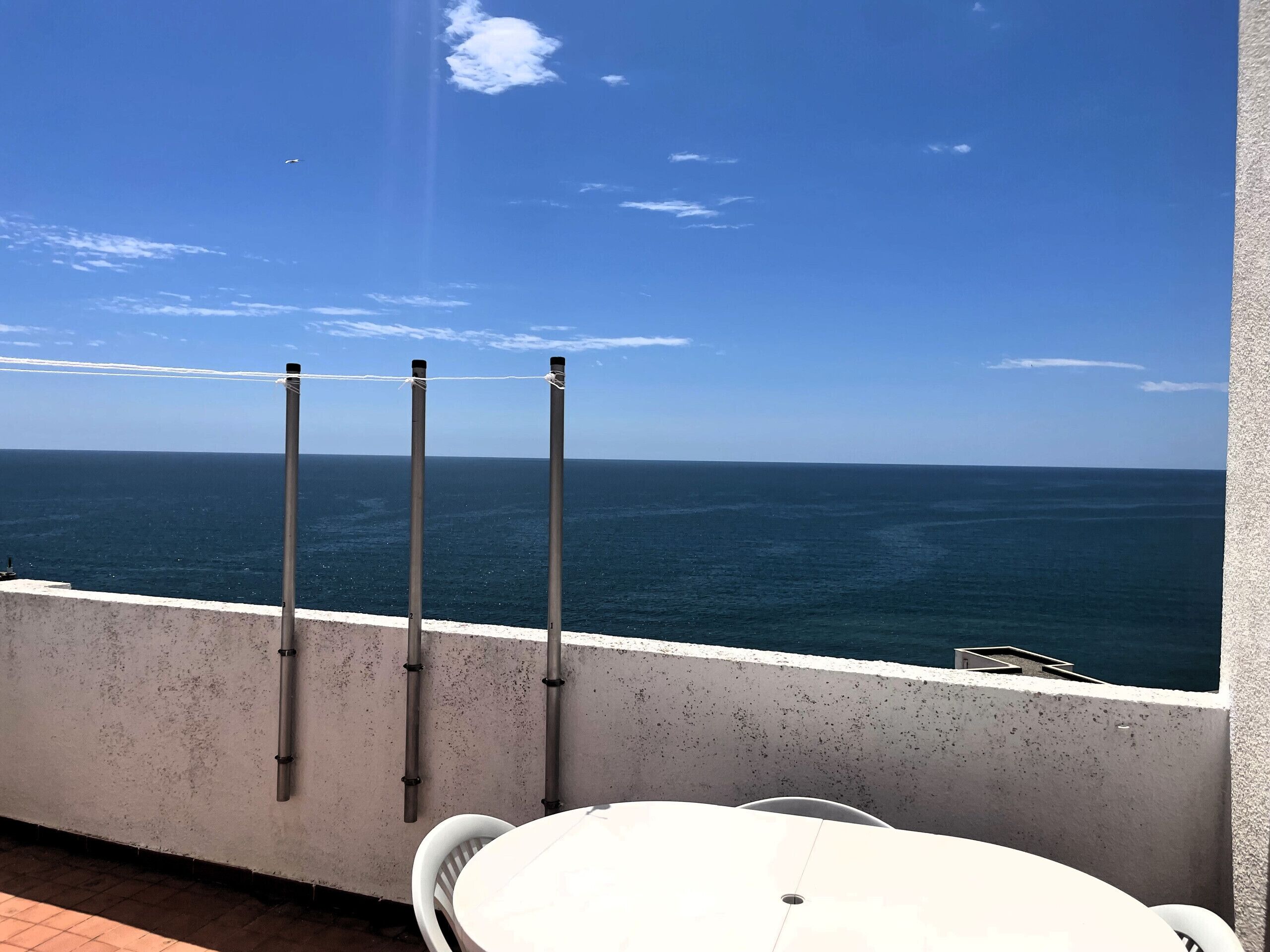 Een balkon met uitzicht op zee, een witte tafel en twee palen.