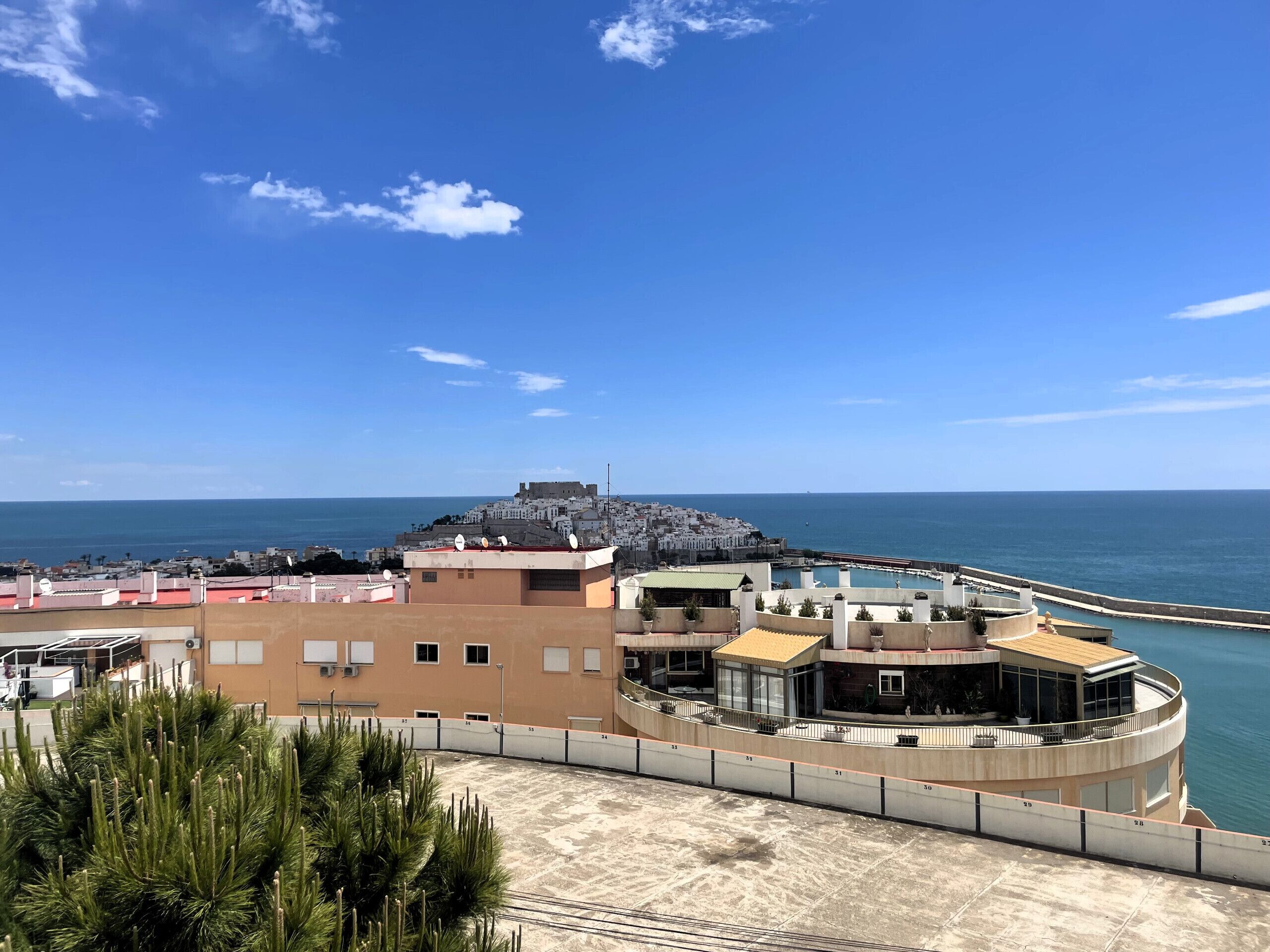 Hotel à beira-mar com piscina, vista para o mar e uma estrutura fortificada ao fundo.