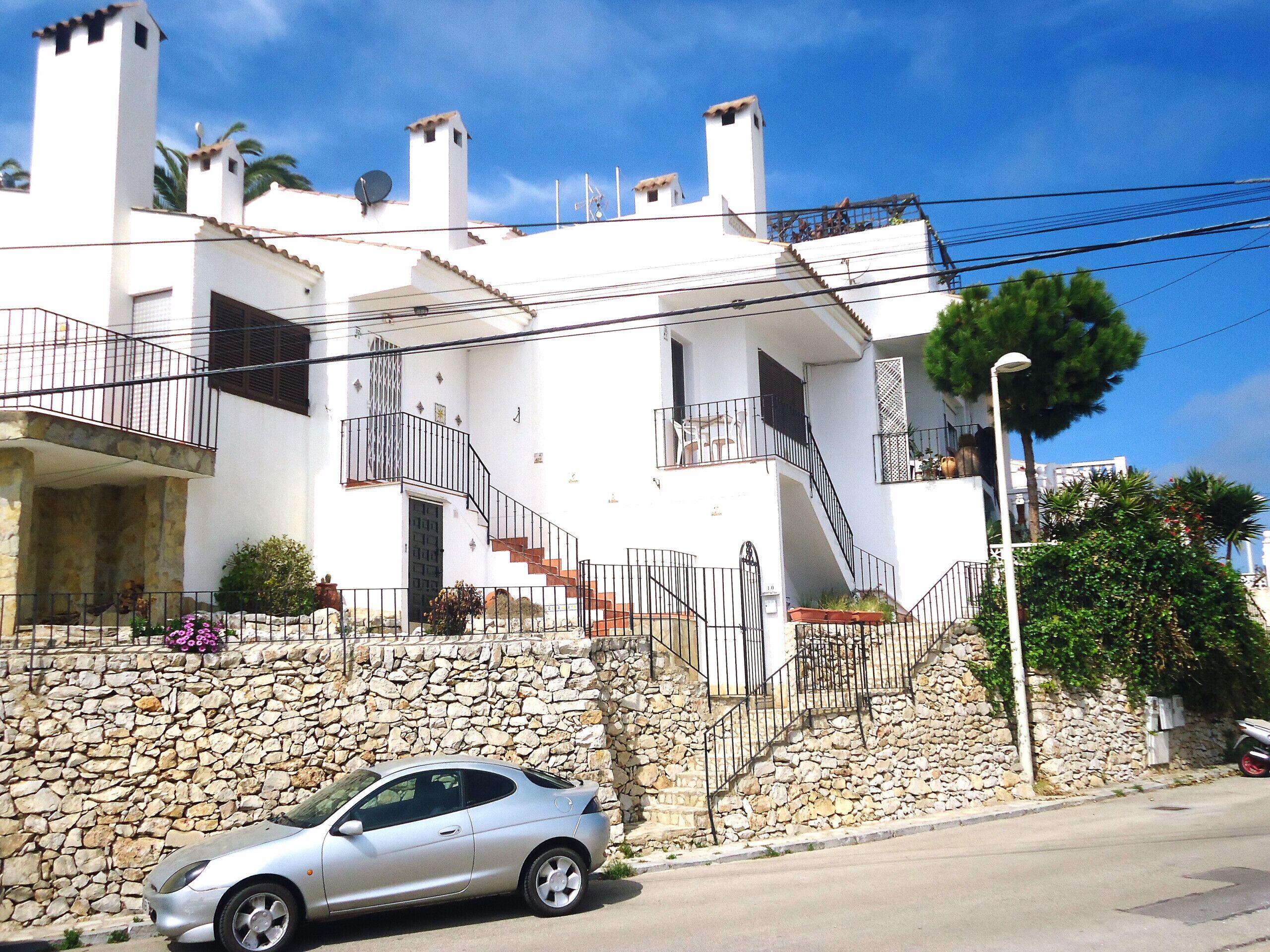 A white building with a stone wall, a staircase, and a parked car.
